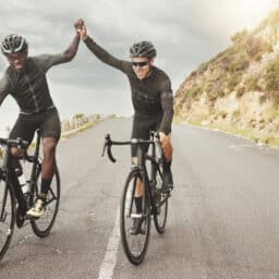 Two men high-fiving as they cycle down a road