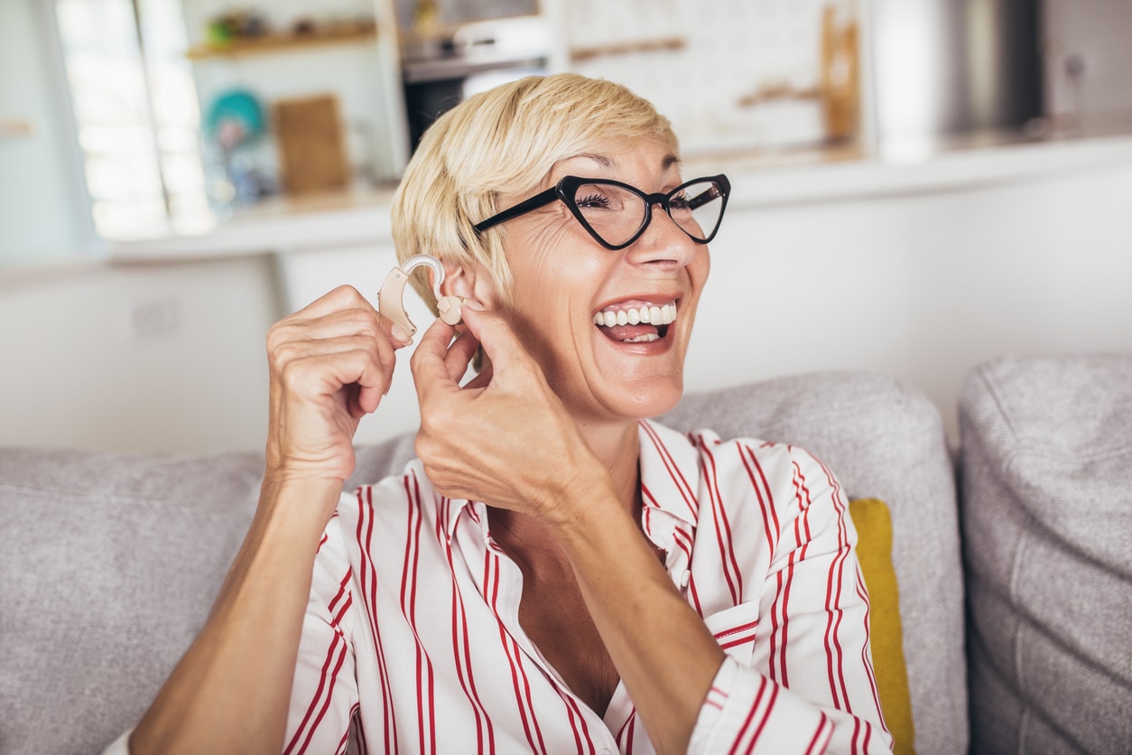 Woman putting in hearing aid looking happy.