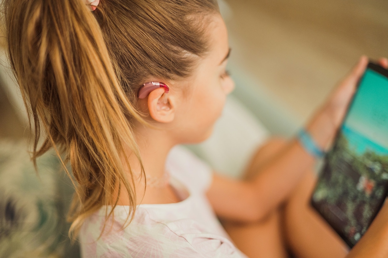 Young girl wearing a hearing aid holding a tablet.