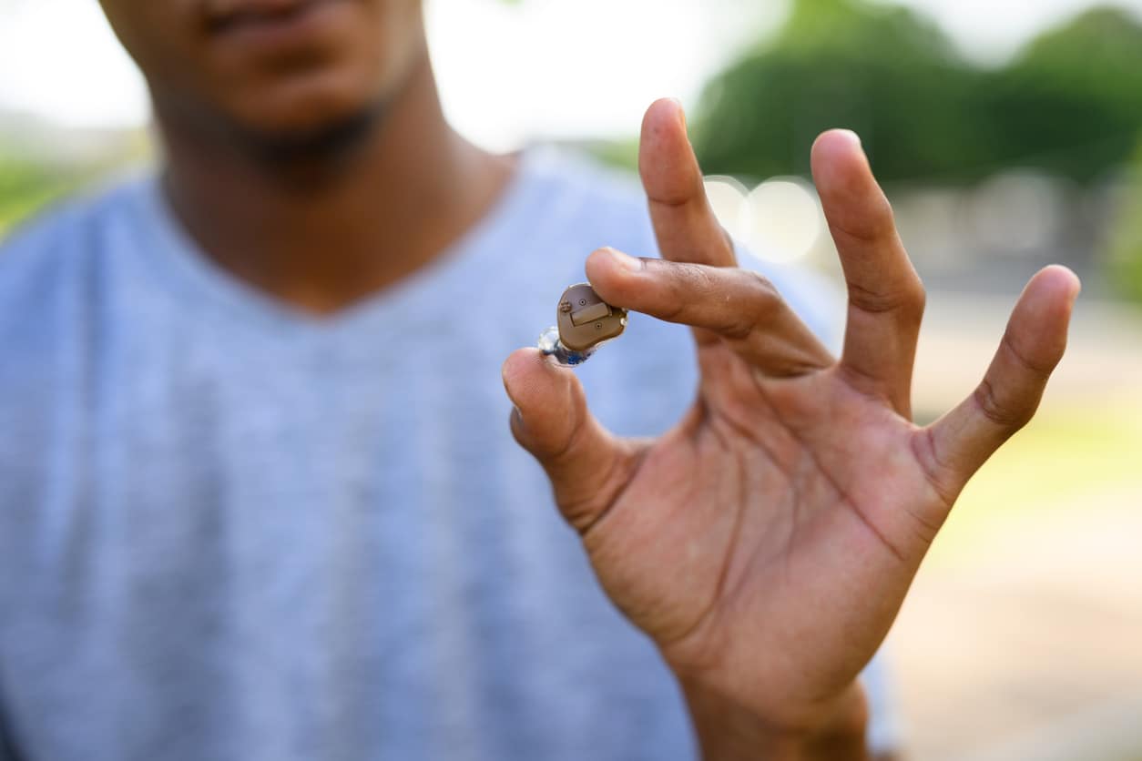 Close up of a man holding a hearing aid.