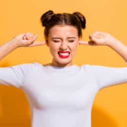 Woman on a yellow background plugging her ears