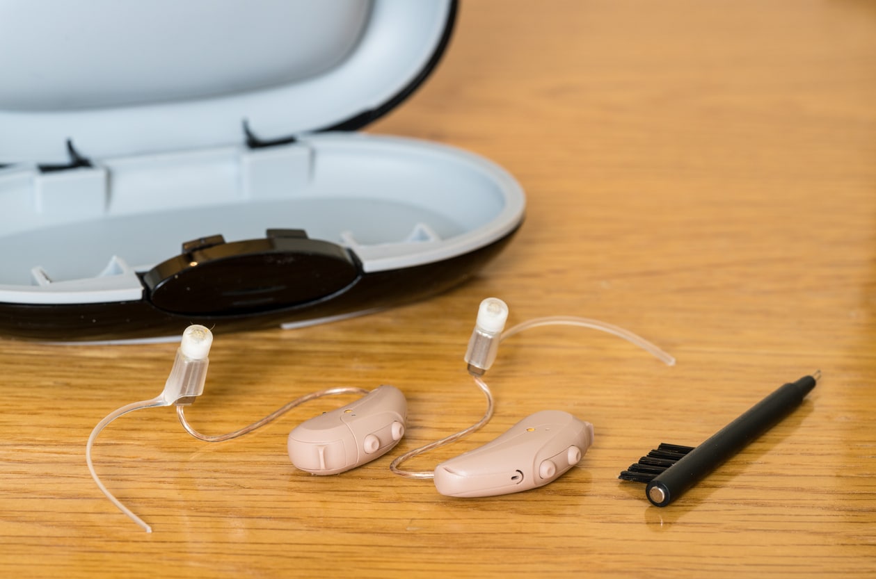 Hearing aids on a table with a cleaning brush and dryer box. 