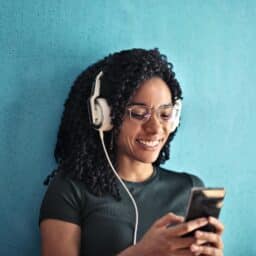 A happy person listens to an audiobook on their phone through headphones.